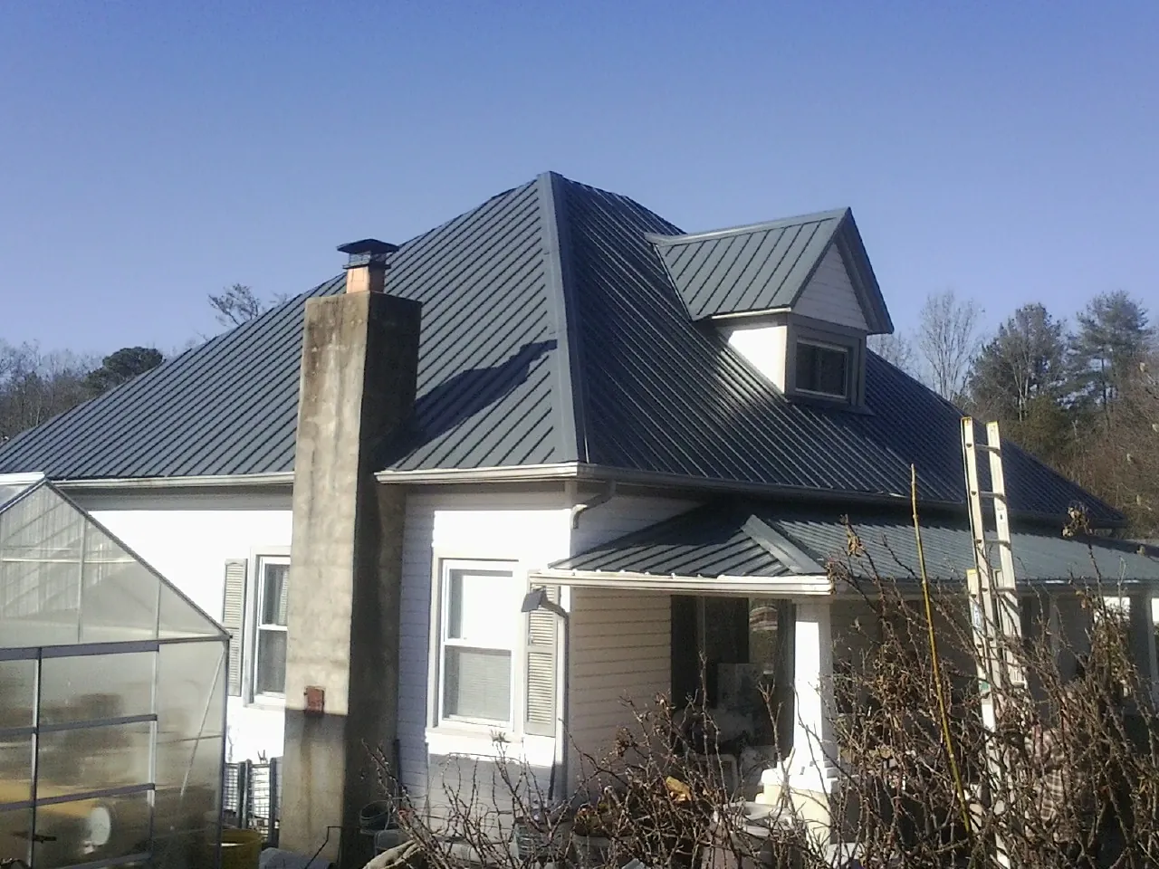 Dark blue standing seam metal roof on a white farmhouse with dormer — Slate & Tile Roof Repair by Roofing Brothers in Bowlus
