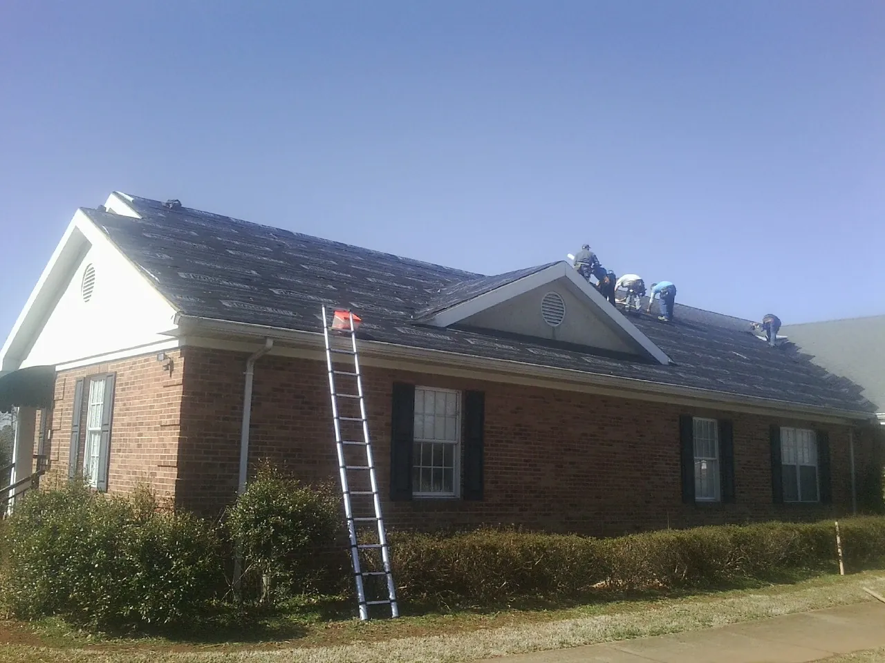 Crew tearing shingles off a brick ranch roof with a ladder set — Emergency Roof Repair work by our crew in Bowlus