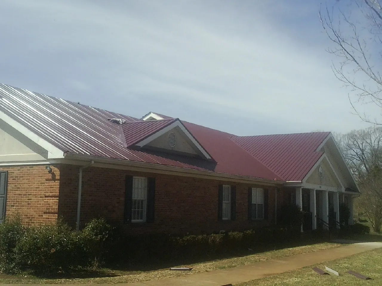 Red metal roof with gabled entries on a long brick building, from a Hail Damage Roof Repair job in Bowlus