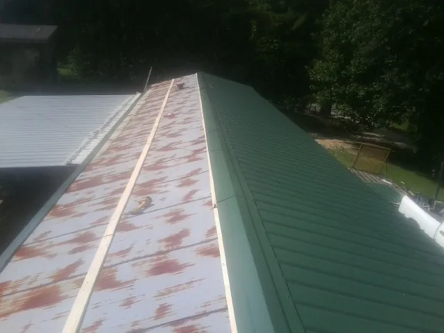 Old rusted panels beside newly installed green metal roofing — Wind Damage Roof Repair by Roofing Brothers in Bowlus