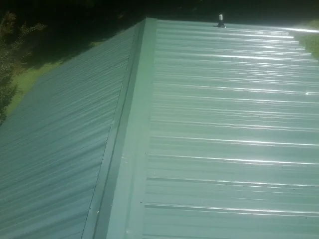 New green metal panels meeting at the ridge of a roof — Flat Roof Repair work by our crew in Bowlus
