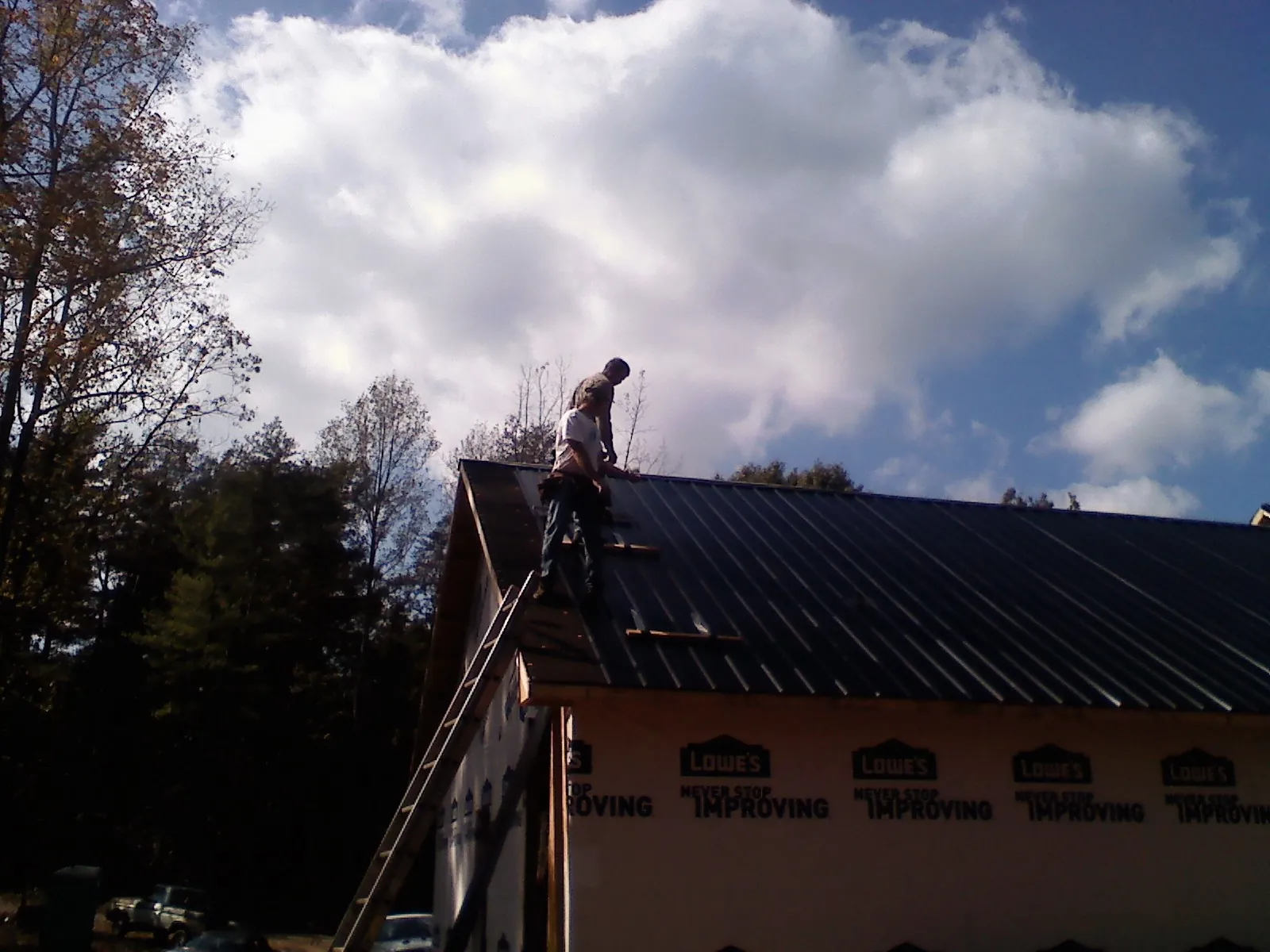 Roofer fastening dark metal panels high against a cloudy sky, from a Roof Inspection job in Bowlus