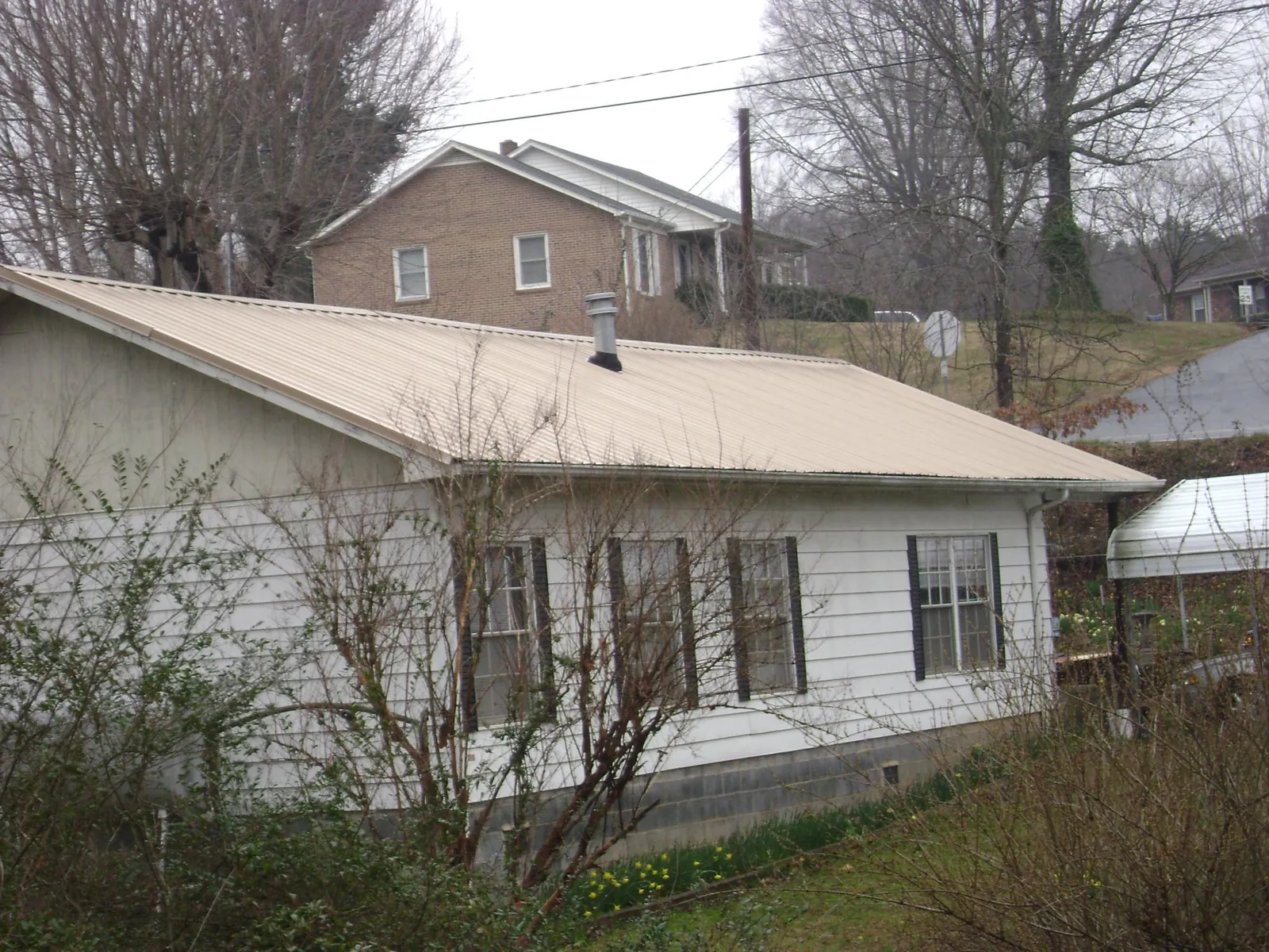 Tan metal roof on a white sided house set into a hillside — Commercial Roofing by Roofing Brothers in Bowlus